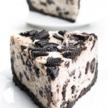 A slice of vegan Oreo cheesecake sits on a plate. Another slice is behind it.
