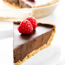 A slice of chocolate pie has raspberries on top. The rest of the pie is behind it.