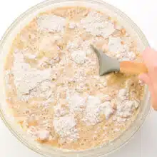 A hand holds a spatula, stirring cake batter in a bowl.